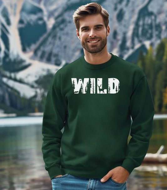 Man wearing a green sweatshirt with 'WILD' printed on it, standing in front of a mountainous landscape.