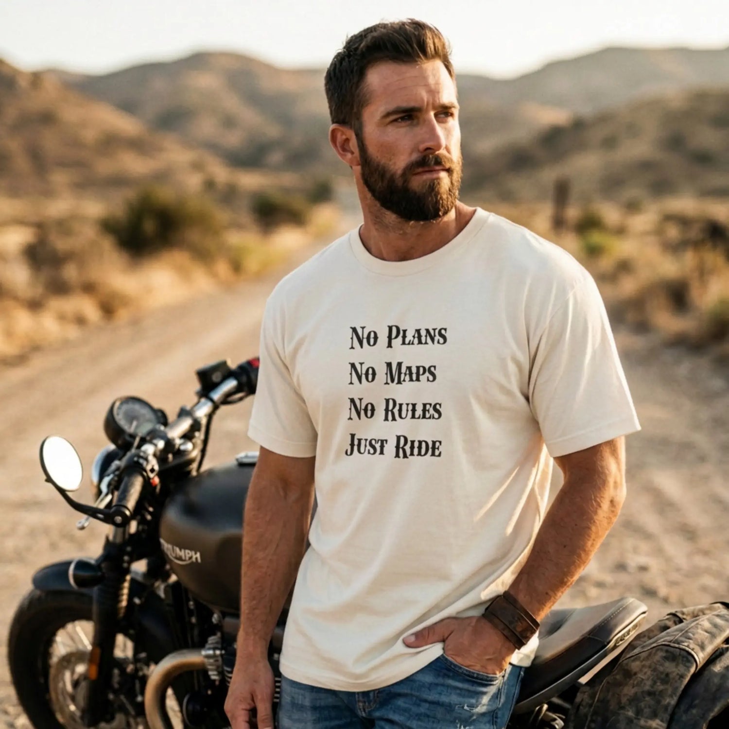 Man standing next to a motorcycle in a desert setting wearing a t-shirt with text.