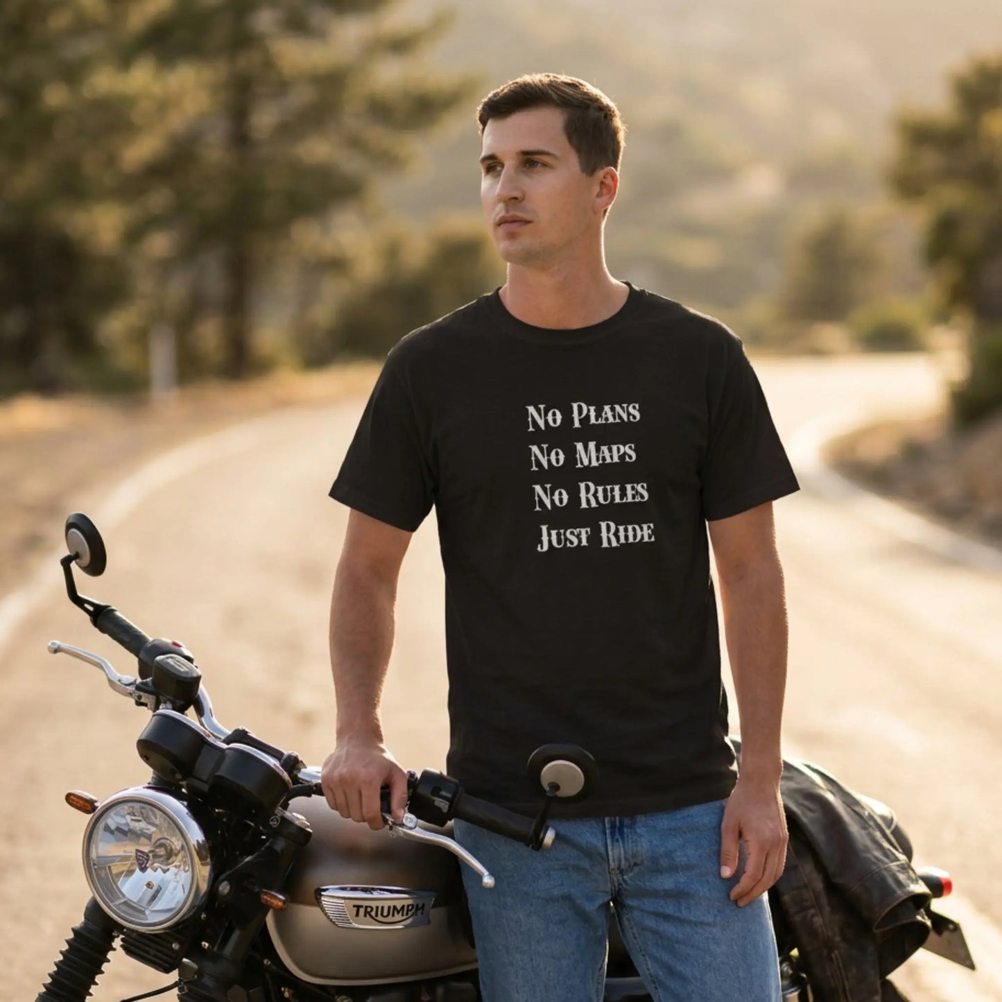Man wearing a black t-shirt with text standing next to a motorcycle on a road with trees in the background