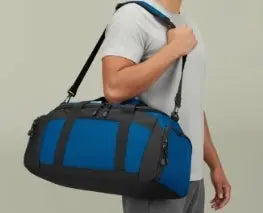 Person carrying a blue and black duffel bag on a plain background